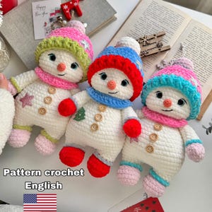 Könnte beinhalten: Drei gehäkelte Schneemann-Puppen mit weißen Körpern, Holzknöpfen sowie bunten Mützen und Schals. Die linke Puppe hat eine rosa-grüne Mütze, die mittlere eine rot-blaue und die rechte eine rosa-blaue Mütze. Der Text lautet Pattern crochet English.