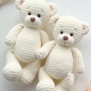 May include: Two white crocheted teddy bears sitting together. The bears have brown eyes and noses.