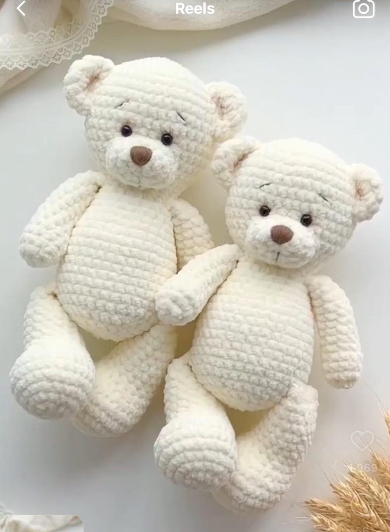 May include: Two white crocheted teddy bears sitting together. The bears have brown eyes and noses.