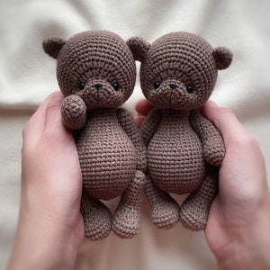Peut inclure: Deux ours en peluche en crochet marron avec des yeux et des nez noirs, tenus dans les mains d'une personne.