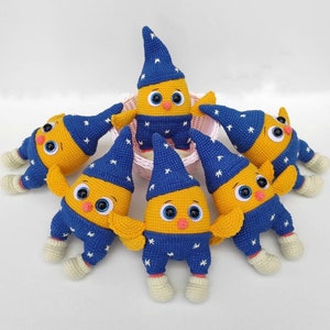 May include: Six crocheted plush toys in the shape of a yellow bird wearing blue pajamas with white stars. The birds are all wearing blue pointed hats with white stars.