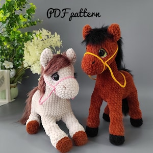 Puede incluir: Dos juguetes de caballos de crochet de felpa. Uno es blanquecino con detalles marrones y una brida rosa. El otro es marrón con detalles negros y una brida amarilla. El texto "PDF pattern" está arriba.