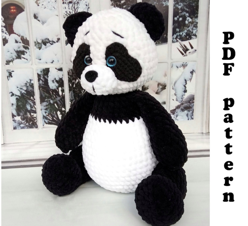Peut inclure: Une peluche panda faite &agrave; la main, avec une fourrure noire et blanche, des yeux bleus et une expression triste. Le panda est assis, avec le texte "PDF pattern" en noir sur le c&ocirc;t&eacute; droit de l'image.