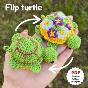 Op de afbeelding: Een handgemaakt, omkeerbaar gehaakt schildpaddenspeelgoed. De ene kant is groen met een bruin ontwerp, de andere is geel met witte, paarse en gele bloemdetails. De tekst "Flip turtle" staat boven het speelgoed.