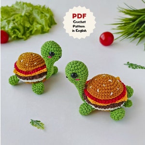 Puede incluir: Dos juguetes amigurumi de tortuga hechos a crochet con un diseño de hamburguesa. Las tortugas son verdes con detalles marrones, amarillos, rojos y blancos. Las tortugas están sobre un fondo blanco.