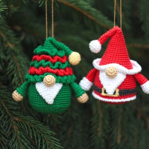May include: Two crocheted gnome ornaments, one green with red and white accents and one red with white and black accents. Both gnomes have white beards and are hanging from a Christmas tree.