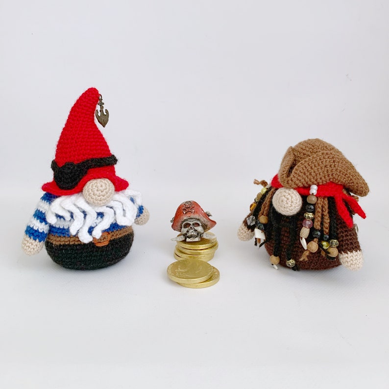 May include: Two crocheted gnomes, one wearing a red hat and blue and white striped shirt, the other wearing a brown hat and a red bandana. Both gnomes have white beards and are holding gold coins.