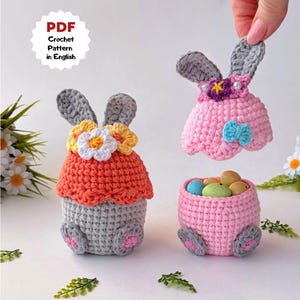 May include: Crocheted Easter bunny decorations in gray, orange, and pink. One bunny is holding a pink dress with a blue bow. Another bunny is holding a basket with colorful eggs. The text "PDF Crochet Pattern in English" is in a white circle.