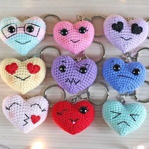 May include: Nine crocheted heart-shaped keychains with different facial expressions. The keychains are in various colors, including pink, blue, yellow, purple, and red.