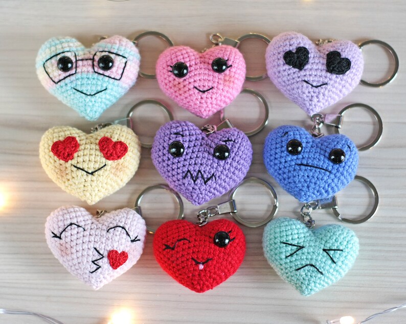 May include: Nine crocheted heart-shaped keychains with different facial expressions. The keychains are in various colors, including pink, blue, yellow, purple, and red.