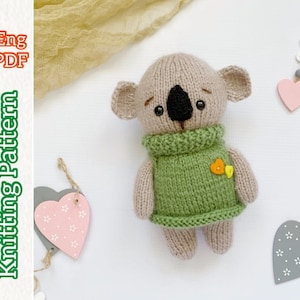Puede incluir: Patrón de tejido para un juguete amigurumi de koala que lleva un suéter verde con una flor amarilla. El patrón está disponible en inglés y es una descarga PDF.