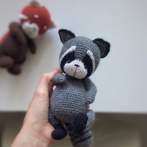 May include: A crocheted raccoon plush toy with a gray body, black eyes, white nose, and black and white striped tail.