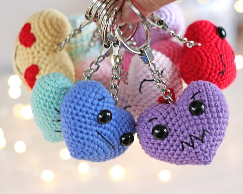 May include: A set of crocheted heart-shaped keychains in various colors, including yellow, green, blue, purple, pink, and red. Each heart has a different facial expression, with embroidered eyes and mouths.