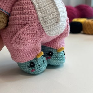 May include: A crocheted unicorn toy with pink and white fur, blue and yellow hooves, and black eyes.