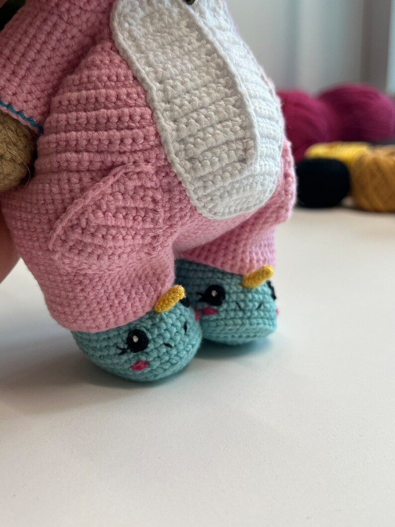 May include: A crocheted unicorn toy with pink and white fur, blue and yellow hooves, and black eyes.