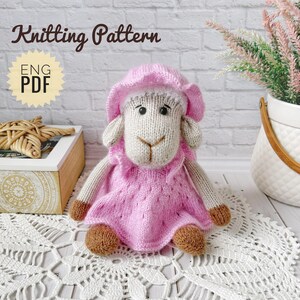 Puede incluir: Un juguete de oveja tejido con un vestido y un gorro rosas. La oveja tiene cara, orejas y patas beiges con pezuñas marrones. La imagen incluye el texto "Knitting Pattern" y "ENG PDF".