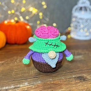 May include: A crocheted Frankenstein monster toy with a pink brain, green stitched-up neck, purple body, and brown shoes.