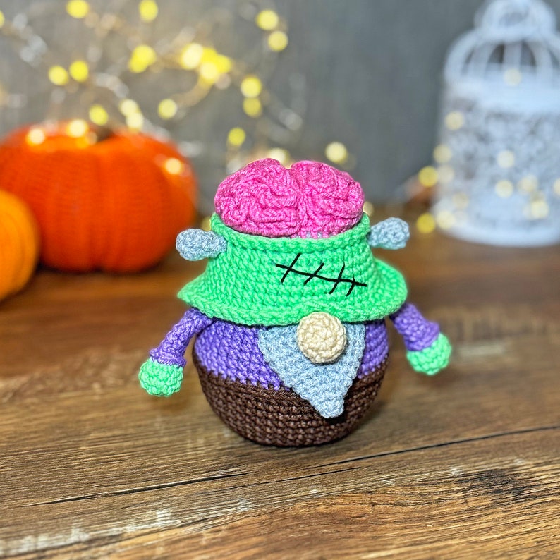 May include: A crocheted Frankenstein monster toy with a pink brain, green stitched-up neck, purple body, and brown shoes.