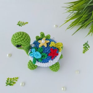 May include: A crocheted green turtle with a blue shell decorated with colorful flowers, leaves, and pearls.