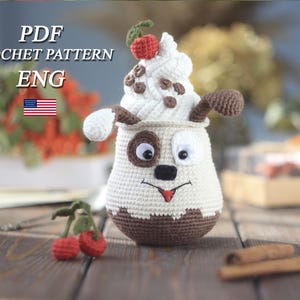 May include: A crocheted dog-shaped container with a white ice cream topping, chocolate chips, and a cherry. The container has brown and white sections, with embroidered facial features. The image includes the text "PDF CROCHET PATTERN ENG" and a US flag.