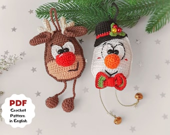 May include: Two handmade crochet Christmas ornaments: a reindeer with a red nose and a snowman wearing a black hat and red bow tie. The reindeer is brown and tan, and the snowman is white with an orange nose. The ornaments are hanging from a green branch.