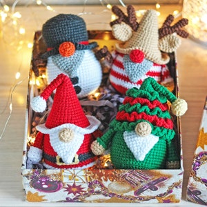 May include: A set of four crocheted Christmas gnomes in a gift box. The gnomes are dressed in red, green, white, and brown. The box is decorated with a Christmas theme.
