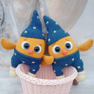May include: Two crocheted stuffed toys shaped like birds with yellow bodies, blue hats, and blue and white striped pants. The toys are sitting in a wicker basket.