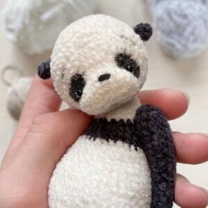 Peut inclure: Un petit ours en peluche panda en crochet avec des yeux noirs et un nez noir. Le panda porte un pull ray&eacute; noir et blanc.