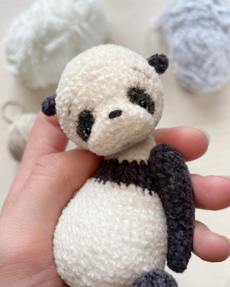Peut inclure: Un petit ours en peluche panda en crochet avec des yeux noirs et un nez noir. Le panda porte un pull ray&eacute; noir et blanc.