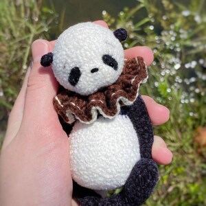 Peut inclure: Un petit ours en peluche panda en crochet avec des yeux noirs, un col &agrave; volants brun et blanc et des pattes en crochet noir.