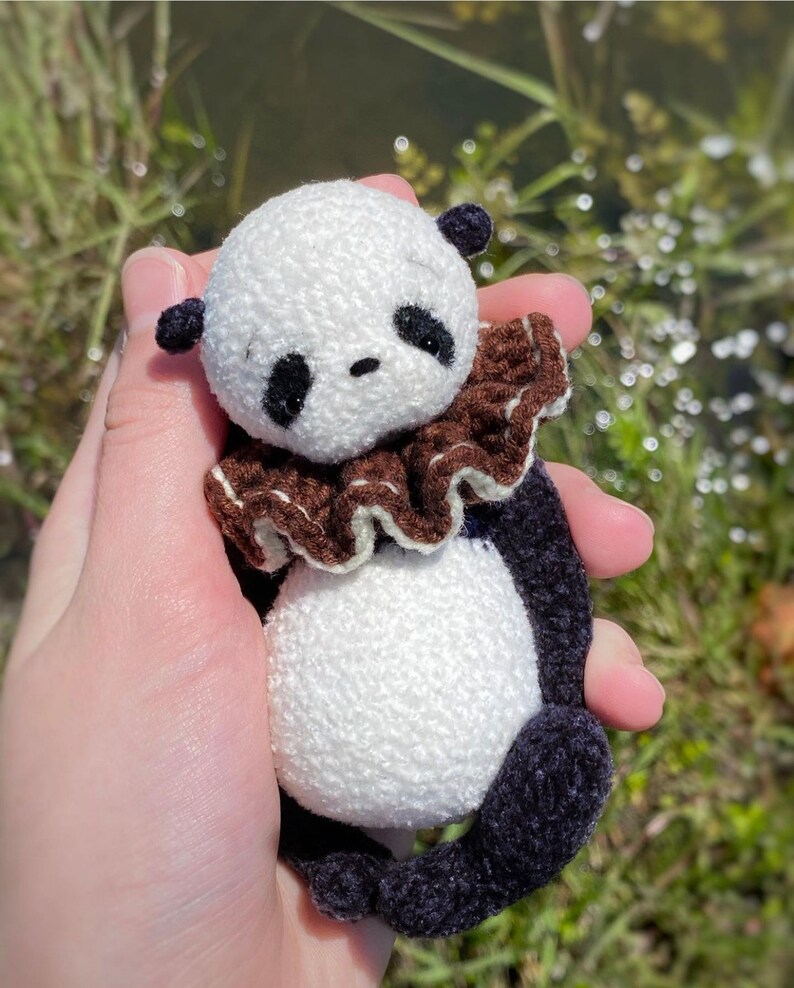 Peut inclure: Un petit ours en peluche panda en crochet avec des yeux noirs, un col &agrave; volants brun et blanc et des pattes en crochet noir.