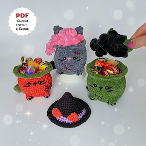 May include: Four crocheted Halloween-themed cat-shaped candy holders. One is gray with a pink brain, one is orange, one is green, and one is black. The black cat is holding a witch's hat.