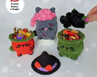 May include: Four crocheted Halloween-themed cat-shaped candy holders. One is gray with a pink brain, one is orange, one is green, and one is black. The black cat is holding a witch's hat.