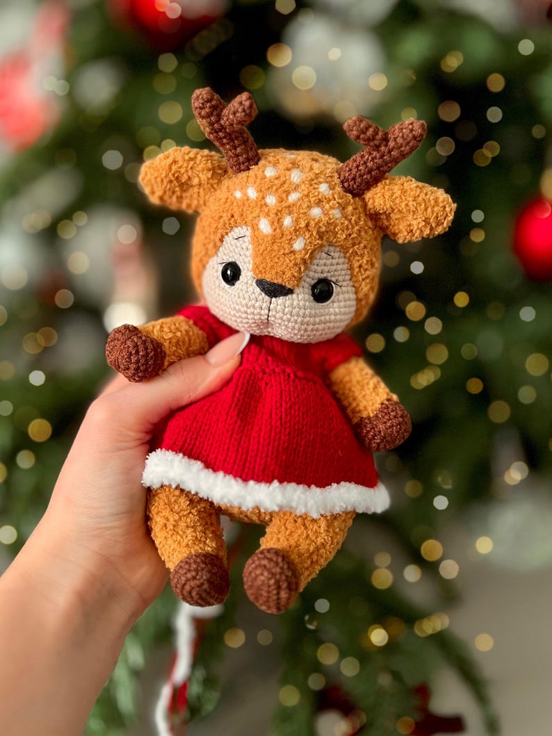 May include: A handmade crochet deer doll with a red dress and white trim. The deer has brown antlers, ears, and hooves, with white spots on its head. The doll is a soft, plush toy.