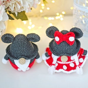 May include: Two crocheted gnomes dressed as Mickey and Minnie Mouse. The Mickey gnome is wearing a black hat with large ears and a red and white polka dot shirt. The Minnie gnome is wearing a black hat with large ears and a red bow, a red and white polka dot dress, and a white trim.
