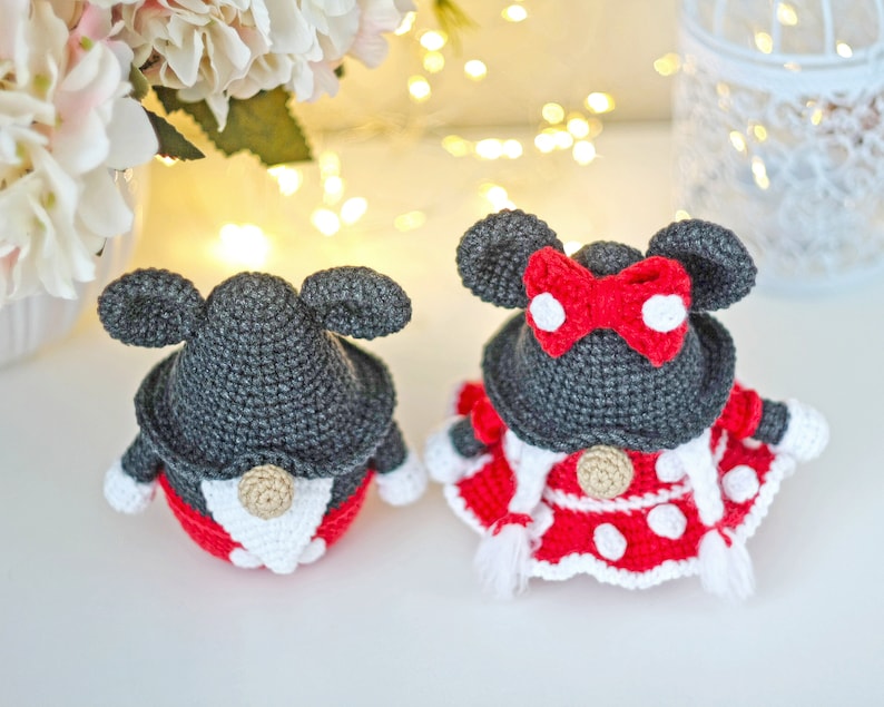 May include: Two crocheted gnomes dressed as Mickey and Minnie Mouse. The Mickey gnome is wearing a black hat with large ears and a red and white polka dot shirt. The Minnie gnome is wearing a black hat with large ears and a red bow, a red and white polka dot dress, and a white trim.