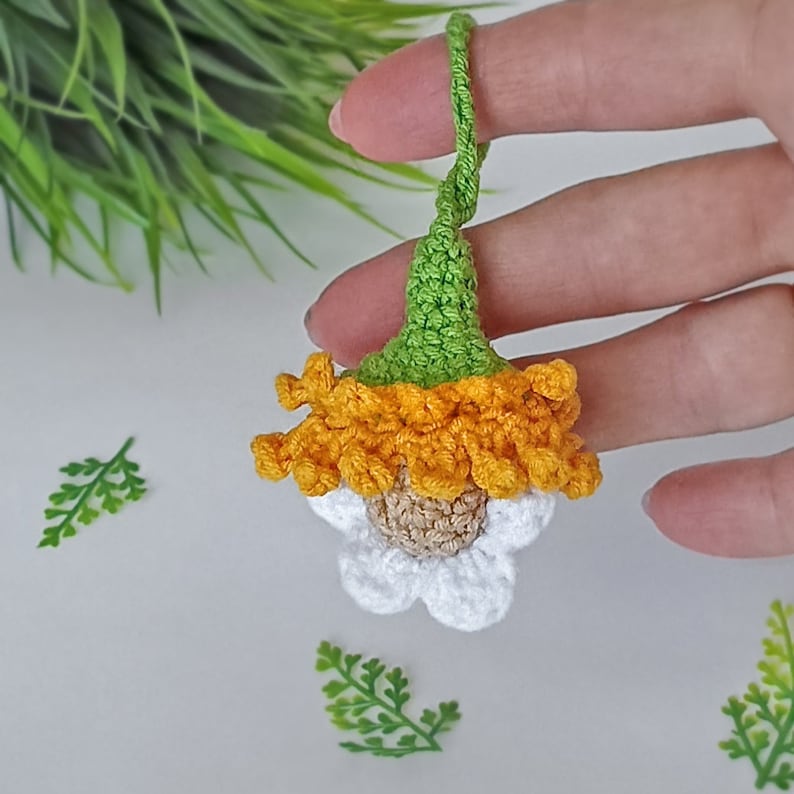 May include: A crocheted flower charm with a green stem, orange petals, and a white center. The flower is hanging from a string.