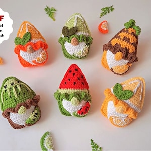 May include: Six crocheted gnomes, each representing a different fruit. The gnomes are made with green, orange, brown, white, and red yarn. The gnomes are sitting on a white surface.  PDF Crochet Pattern in English.