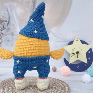 May include: A crocheted stuffed toy shaped like a person wearing a blue hat with white stars and blue pants with white stars. The toy is standing on a brown surface.