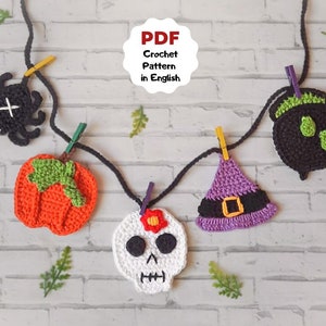 Könnte beinhalten: Eine Halloween-Girlande mit gehäkelten Dekorationen, darunter ein Kürbis, ein Hexenhut, ein Kessel, ein Schädel und eine Spinne. Die Girlande ist an einer schwarzen Schnur befestigt und mit Wäscheklammern aufgehängt.