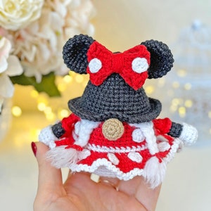 May include: A crocheted gnome doll with a red and white dress, black hat, and red bow with white polka dots. The gnome is holding a white and red striped bag.