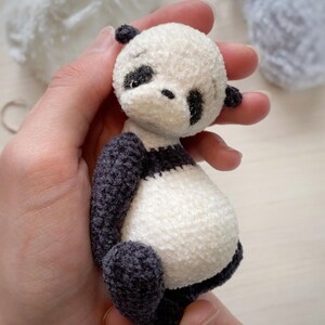 Peut inclure: Un petit ours en peluche panda en crochet avec une fourrure noire et blanche. Le panda a des yeux noirs et un nez noir.
