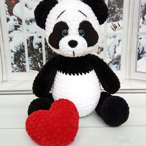 Peut inclure: Une peluche panda faite &agrave; la main, avec une fourrure noire et blanche, des yeux bleus et un c&oelig;ur rouge. Le panda est assis, avec le c&oelig;ur devant lui. En arri&egrave;re-plan, une fen&ecirc;tre avec une sc&egrave;ne enneig&eacute;e.