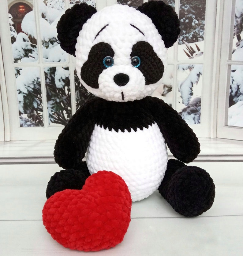 Peut inclure: Une peluche panda faite &agrave; la main, avec une fourrure noire et blanche, des yeux bleus et un c&oelig;ur rouge. Le panda est assis, avec le c&oelig;ur devant lui. En arri&egrave;re-plan, une fen&ecirc;tre avec une sc&egrave;ne enneig&eacute;e.