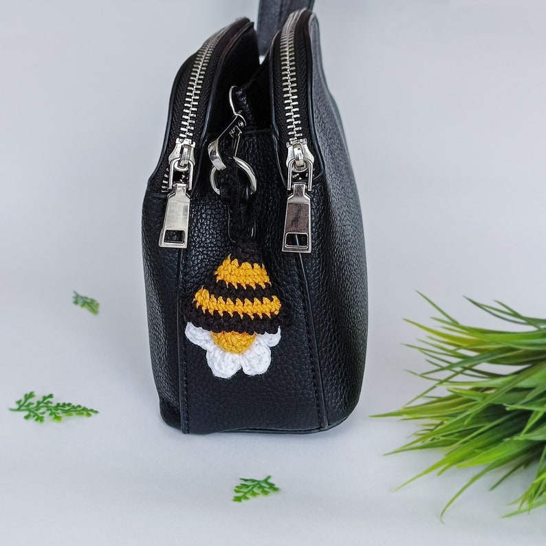May include: Black leather handbag with a crocheted bee charm. The bag has two zipper closures and a silver chain strap.