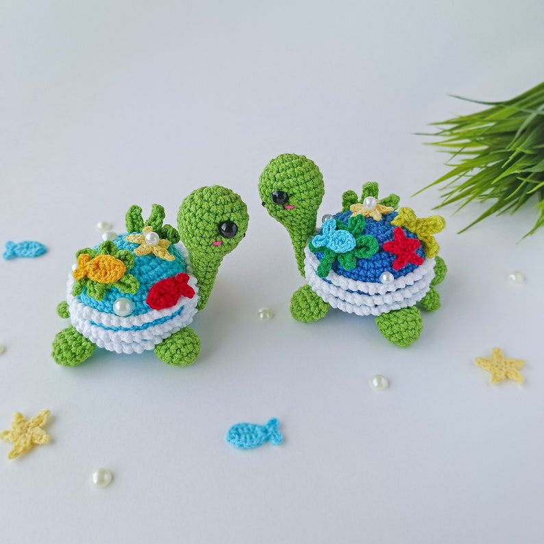 May include: Two crocheted sea turtle toys with colorful details, including flowers, fish, and starfish. The turtles are green with white and blue shells.
