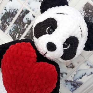 Peut inclure: Une peluche panda faite &agrave; la main, avec une fourrure noire et blanche, tenant un grand c&oelig;ur rouge. Le panda a des yeux noirs et un nez noir. Le jouet est fait d'une mati&egrave;re douce et textur&eacute;e.