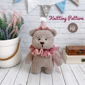 Puede incluir: Un oso de peluche tejido con un cuello de volantes rosa y un sombrero a juego con un pompón blanco. El oso es de color marrón claro y tiene una nariz y ojos cosidos. El texto "Knitting Pattern" y "ENG PDF" es visible.