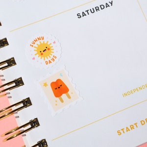 Pu&ograve; includere: Una pagina di un planner bianca con la parola "SABATO" stampata in nero nella parte superiore. Due adesivi sono posizionati sulla pagina. Il primo adesivo &egrave; un adesivo rotondo con un sole giallo con un viso sorridente e le parole "SUNNY DAYS" stampate in nero. Il secondo adesivo &egrave; un adesivo quadrato con un ghiacciolo arancione dei cartoni animati con un viso sorridente.