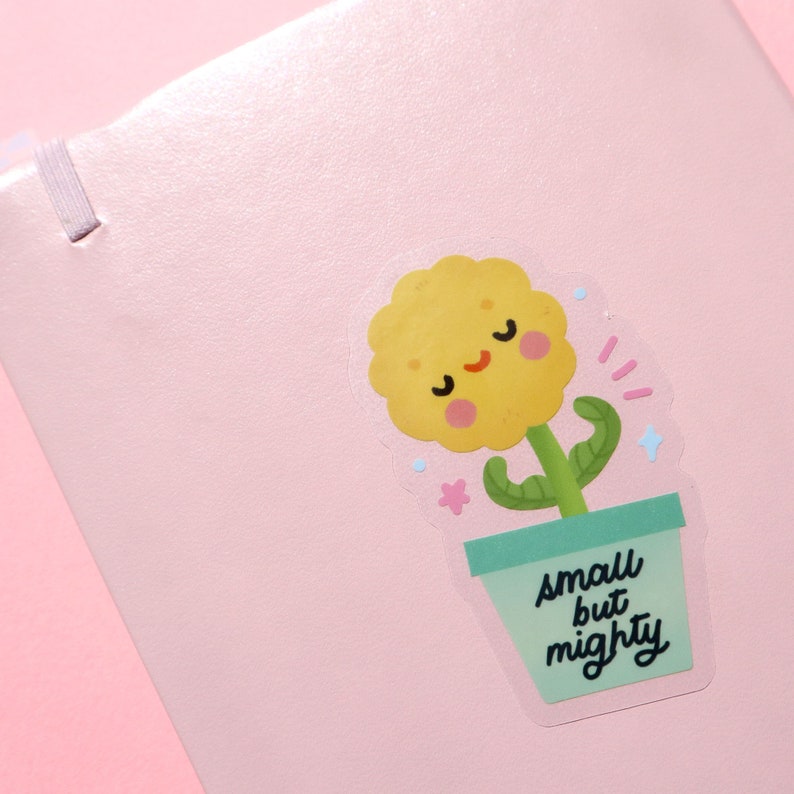 May include: A yellow flower with a smiling face in a green pot with the text "small but mighty" on a pink background.